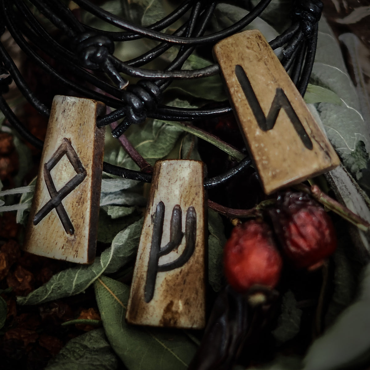 Handmade rune pendant with several bone pendants carved with Nordic runes. Black leather strap. Photographed on natural moss background in forest interior. Traditional Viking-inspired jewelry.