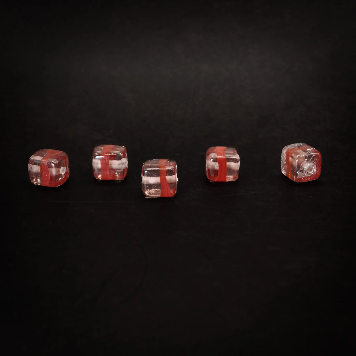 Fem rosa kubiska glaspärlor med röda rander, alternativ produktvinkel mot svart bakgrund