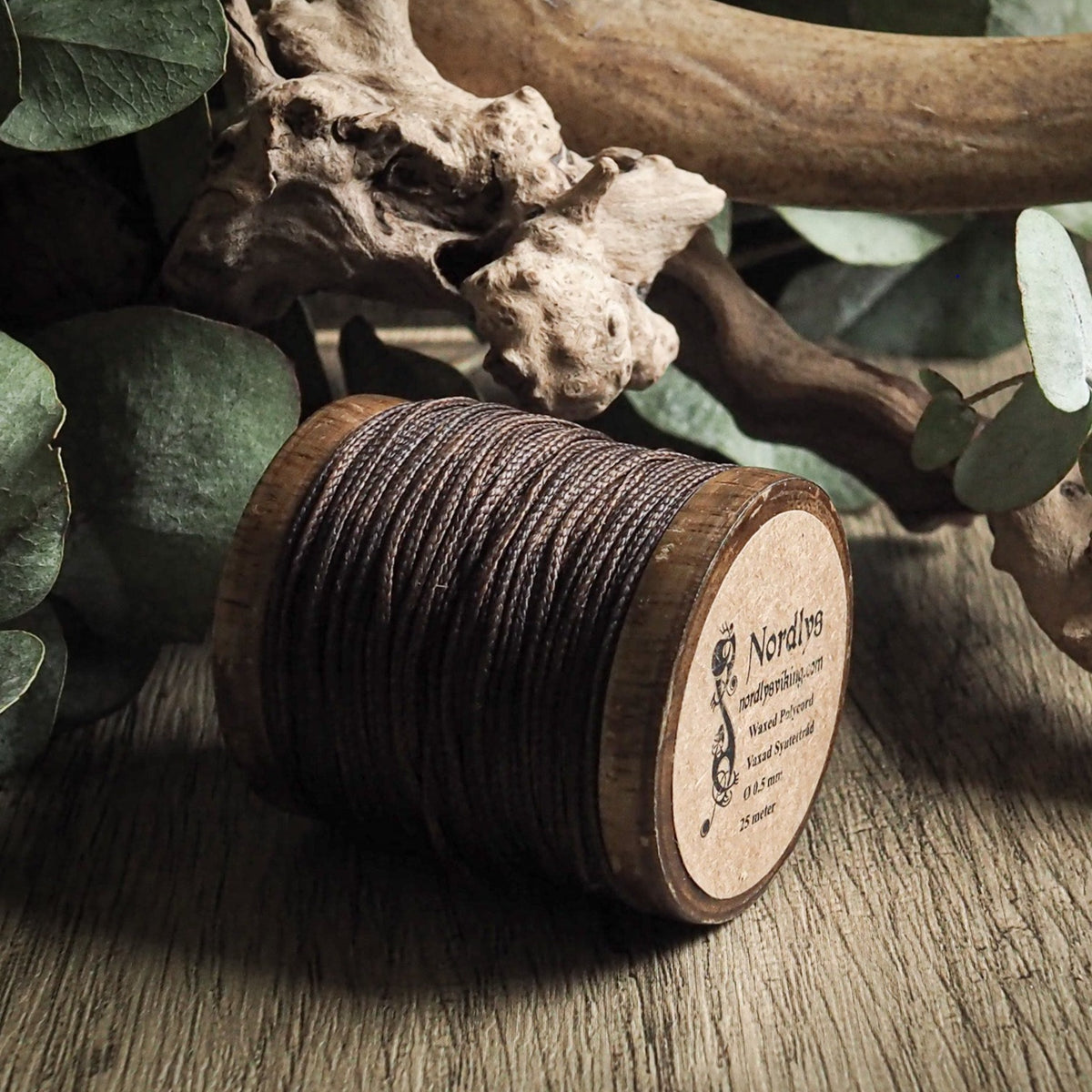 Vaxad sytråd brun på träspole i naturlig miljö med drivved och eukalyptus.