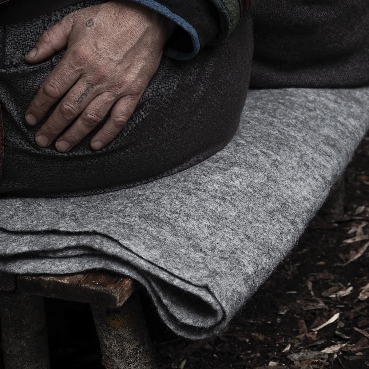 Felted wool blanket, sleeping mat – folded blanket in grey wool on a bench outdoors