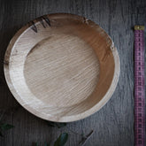 Large disposable palm leaf plate on gray wood, photographed from above with measuring ruler for size reference.