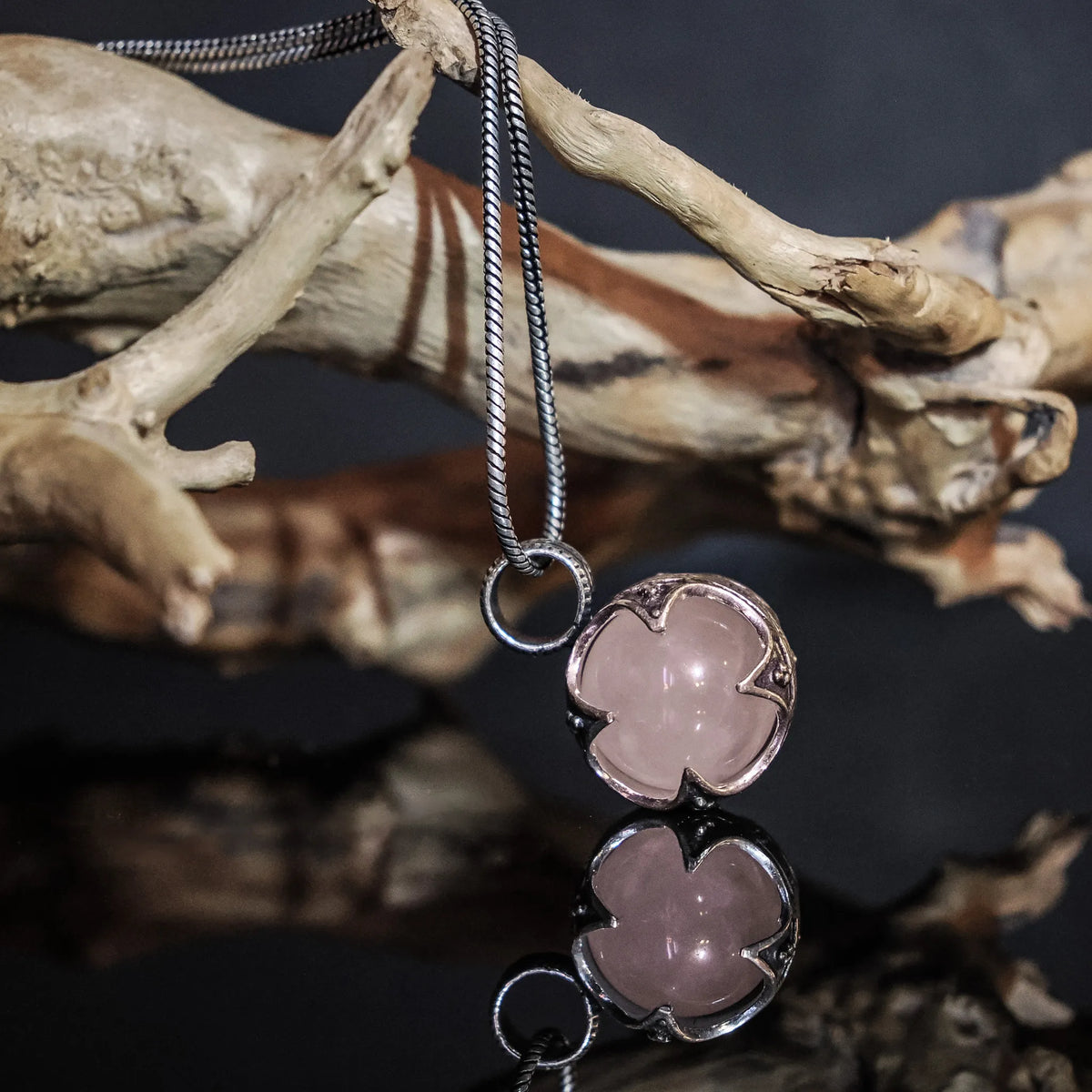 Gotlandshänge-hänge hängande på kedja och presenterad på en trädgren. Rosa kvarts i mässingram med vikinginspirerad dekoration. Visar hur smycket kan bäras.