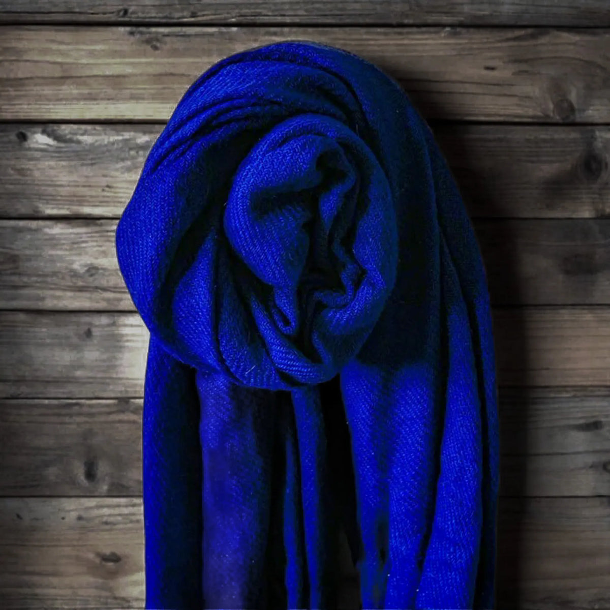 Cashmere shawl, Cornflower blue – the shawl rolled into a rosette, hung against a wooden wall