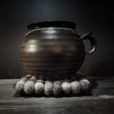 Felted coaster, pack of 4 – a dark clay pot in use on top of the coaster