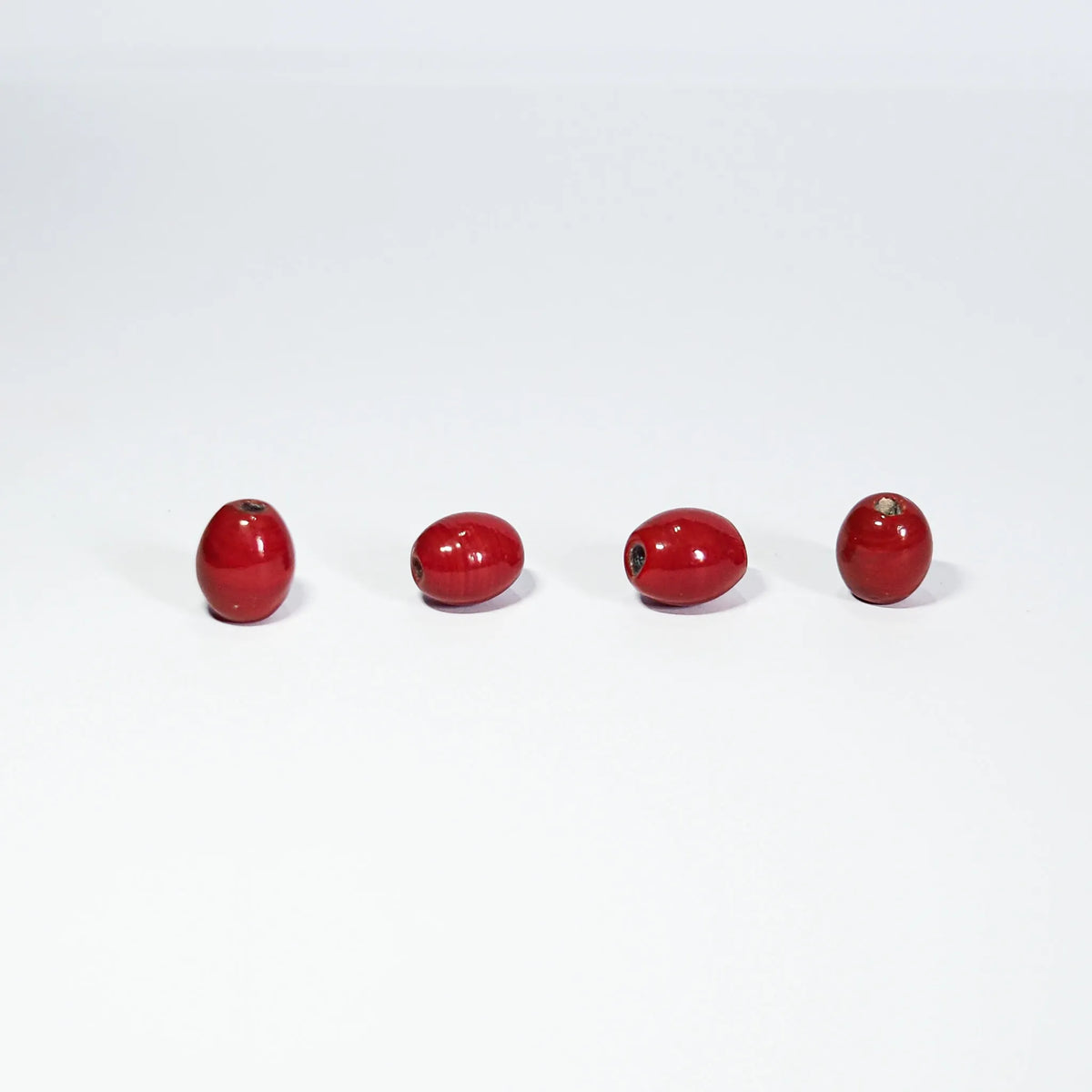 Oval red glass bead – four beads on a light background