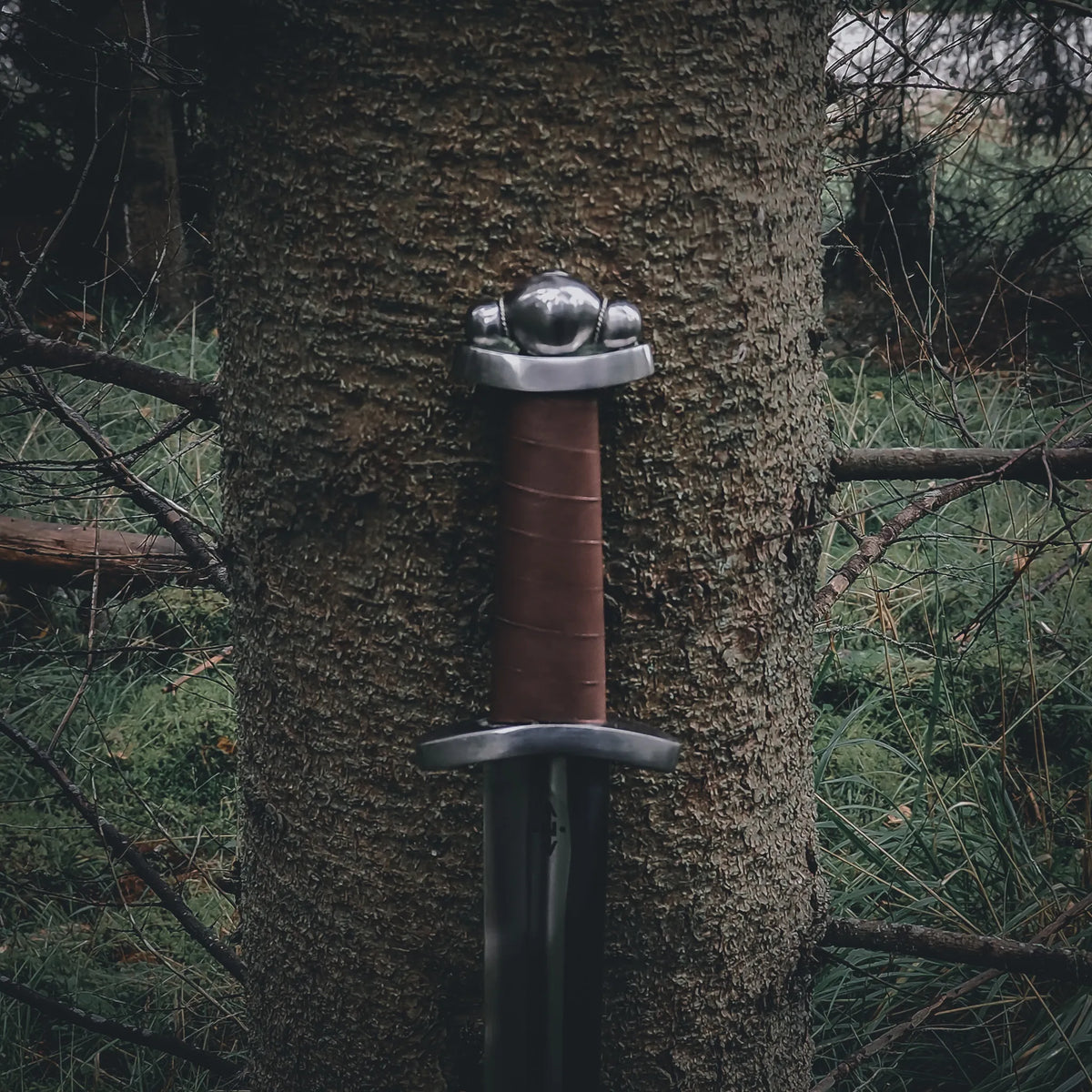 Lofotr Viking sword – pommel and hilt against mossy bark, seen from below