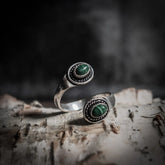 Spiralring med labradorit halvädel som reflekterar norrskenets aurora i blått och grönt, på weathered trä med mässing och dekorativ betoning.