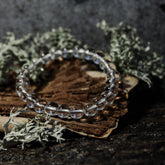 Armband stenpärlor - Tigeröga variant med bergkristall. Elastiskt armband med klara polerade kristallpärlor som speglar ljus, på rustik träbas med mossbeväxt stenbackgrund.
