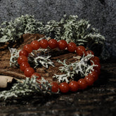Stone bead bracelet - Tiger's eye variant with carnelian. Elastic bracelet with red polished carnelian beads on rustic wood base with mossy stone background.