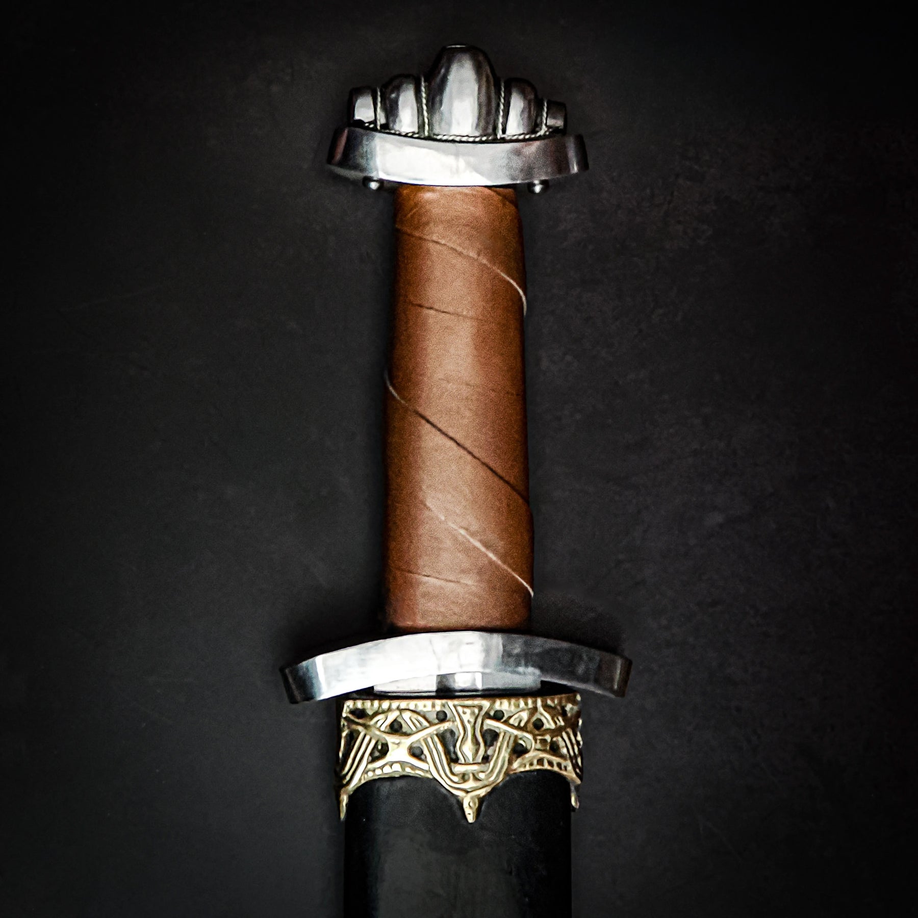 Five Lobed Viking sword – close-up of the five-lobed pommel and the brown-wrapped grip at the scabbard mouth
