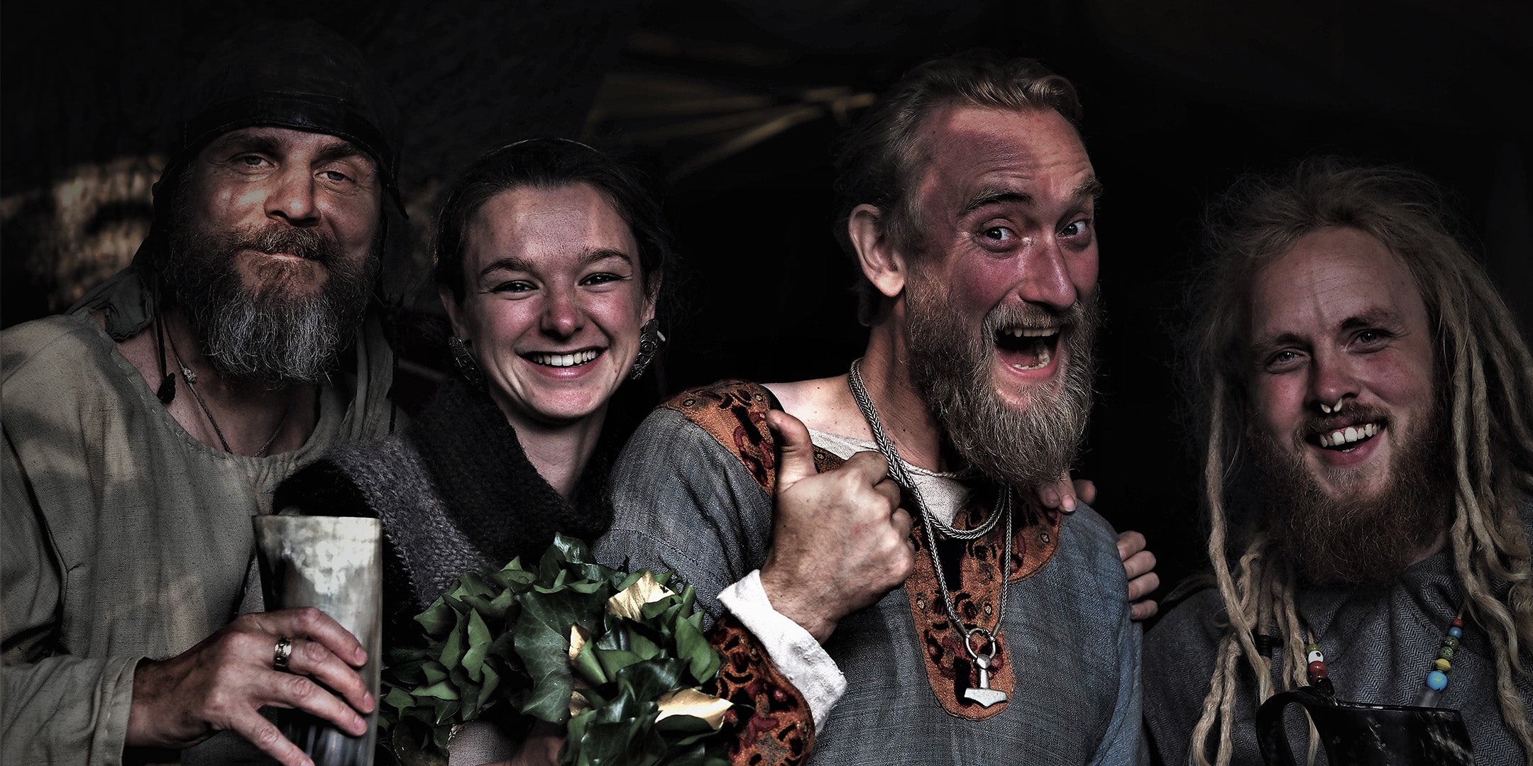 Fyra glada människor i vikingakläder. Alla ler, den ena visar tummel upp
