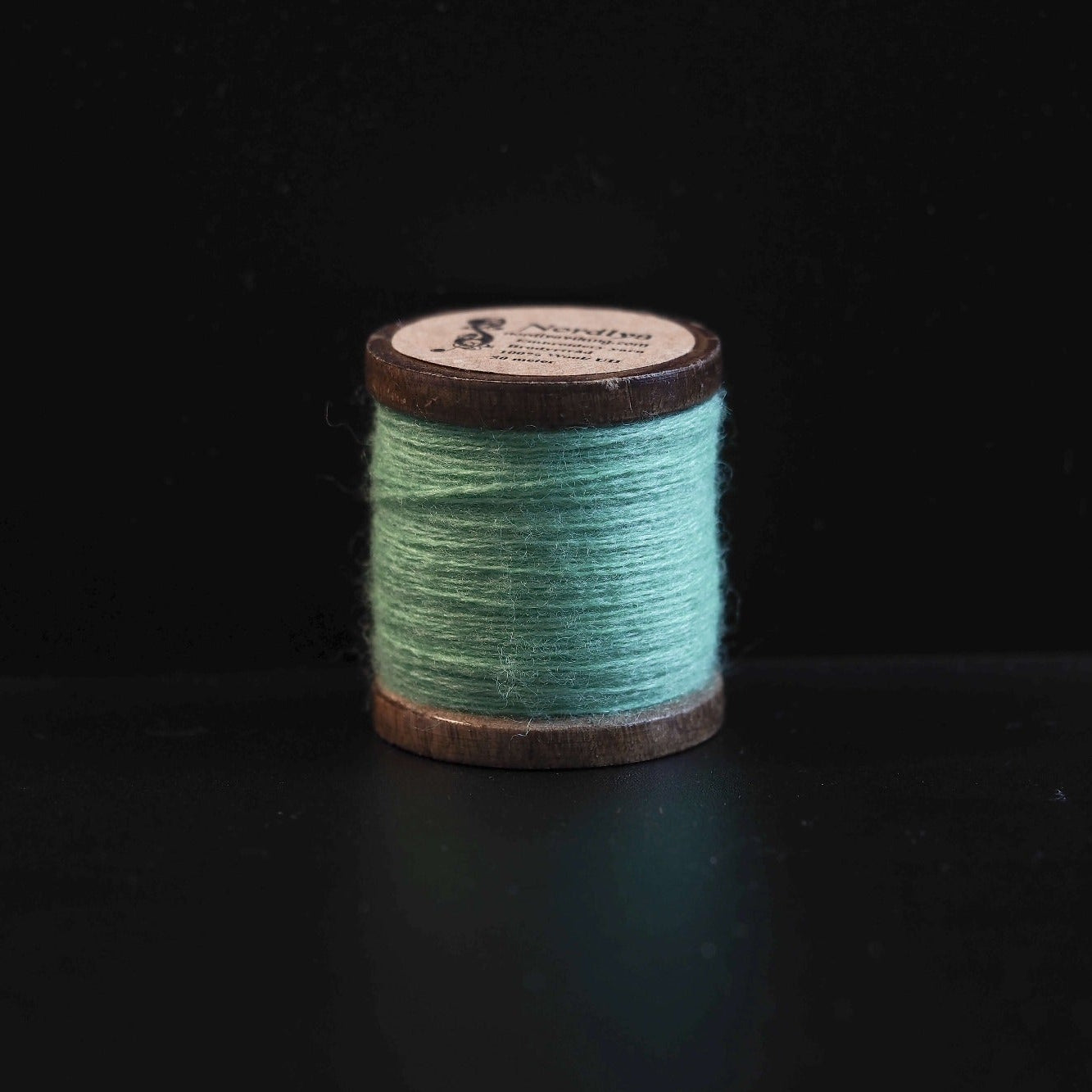 Svart brodertråd på trätrumlor med Nordlys-logga. Klassisk färg för traditionell Viking-inspirerad broderi och formell skandinavisk textilkonst.