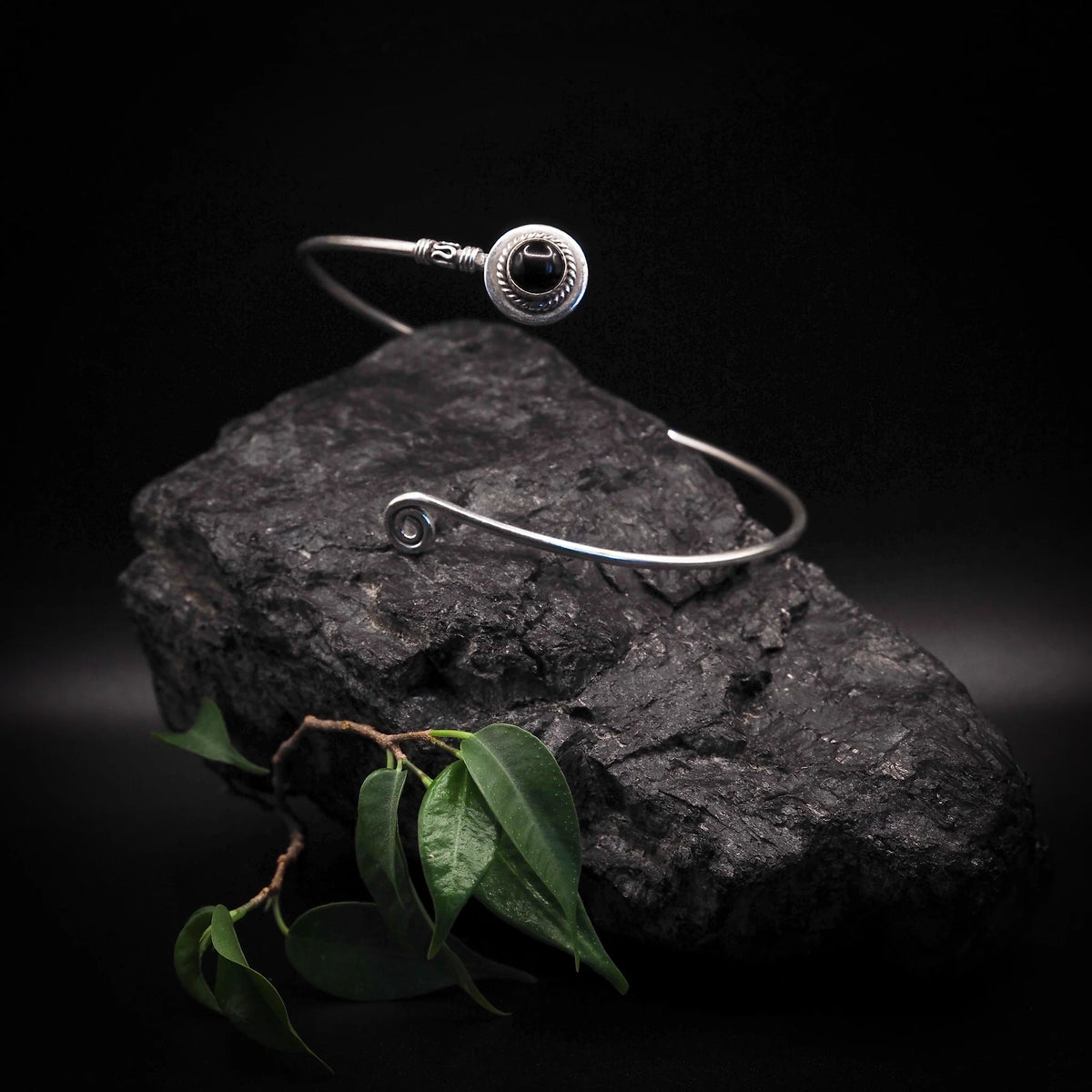 Överarmsring med halvädelsten – svart sten i ringen, ställd mot mörk sten med gröna blad