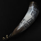 Dryckeshorn vinkelshot visar Torshammare-gravyr i mitten omgiven av norska runor. Organiskt horn med mässing och vikingartsdesign.