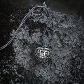 Silverpläterad hjärtformad berlock med detaljerat filigranmönster och ornamental snirkelmönster på strukturerad grå sten.