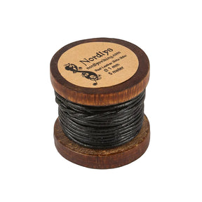 Nordlys läderband 5 meter på träspole fotograferat framifrån mot grå bakgrund. Träspolen med präglat varumärke och text på toppen. Svart lädersnöre lindadt tätt runt spolen.