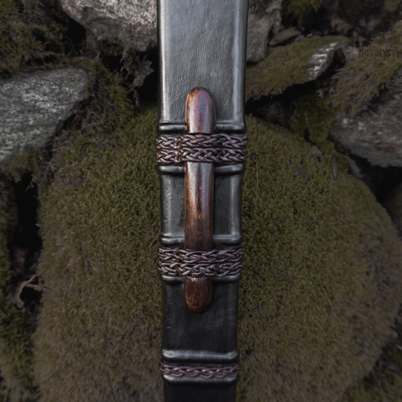 Svärdskida detalj - närbild på läderslida med flätade metallband och trähandtag, vikingatida design